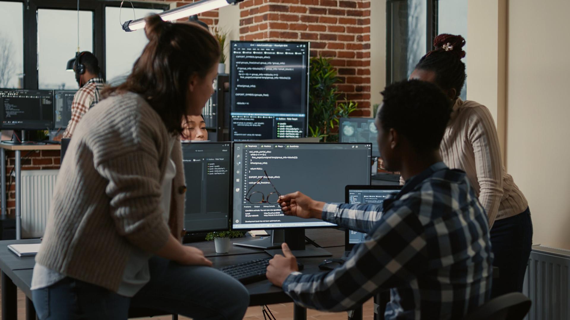 Group of data professionals sit in front of a computer screen while one of them points